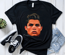 Black t-shirt with a graphic of a famous person, paired with sneakers and jeans on a wooden surface.